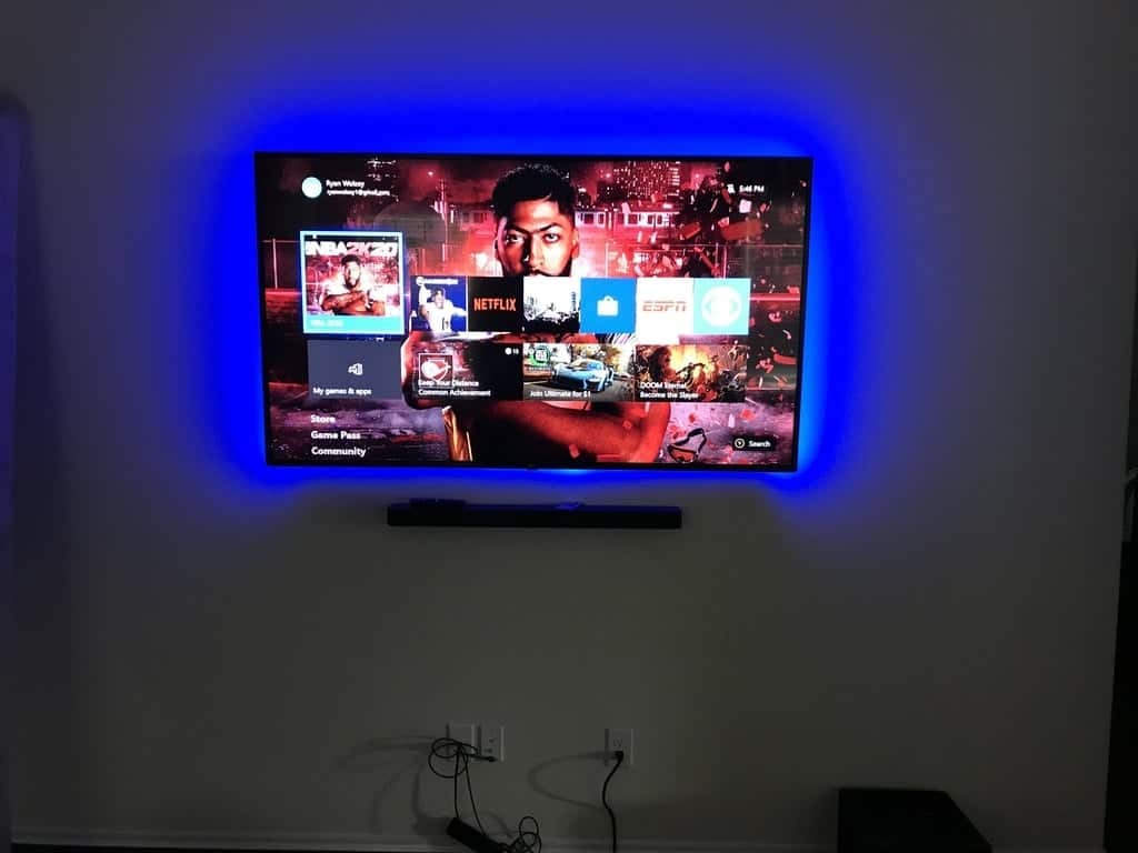 Wall-mounted TV with blue LED backlighting displaying an Xbox home screen
